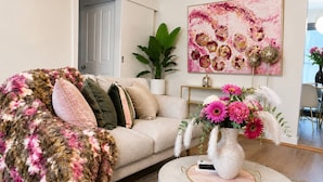 Ein Wohnzimmer mit einer Couch, einem runden Couchtisch, einer Vase mit Blumen und einem Gemälde an der Wand.