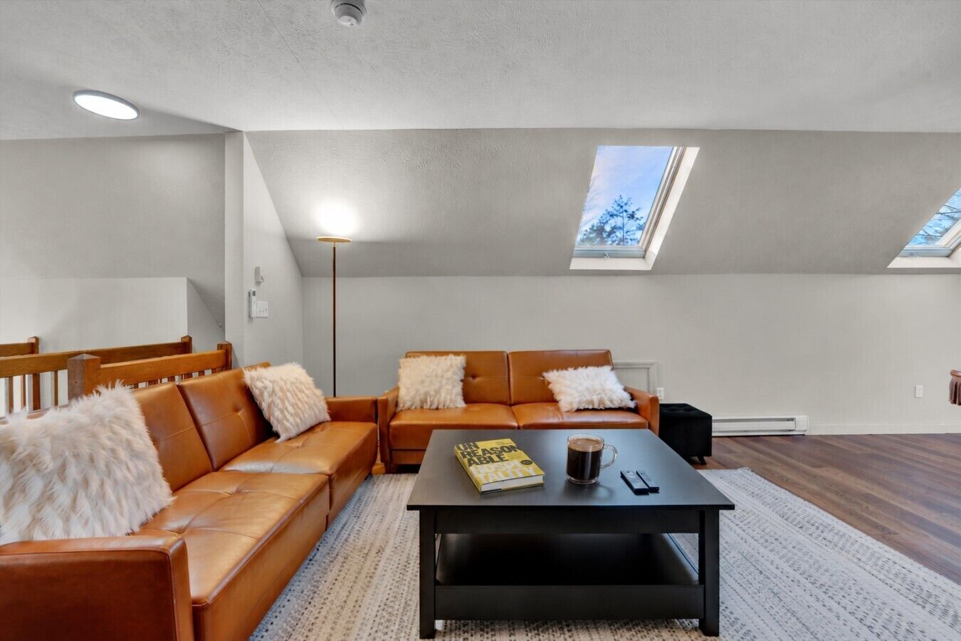 Un salon moderne avec un ensemble de canapés, une table basse et un lampadaire. Le plafond est doté de lucarnes.