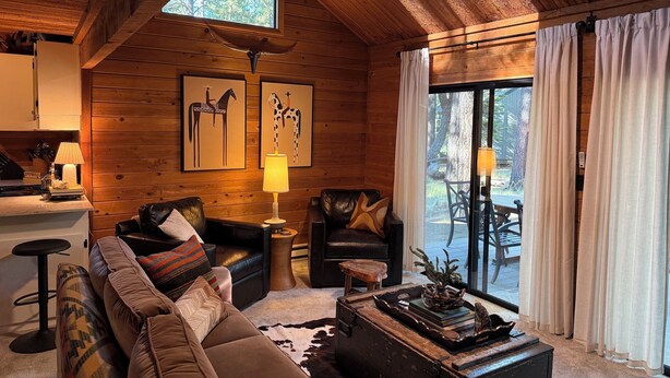 Ein gemütliches Blockhaus-Interieur mit Holzbalkendecke, einer Couch, einem Esstisch und einem großen Fenster.