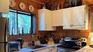 Eine Küche mit Holzboden, weißen Schränken, Edelstahlgeräten und einem Fenster mit Blick auf Bäume.