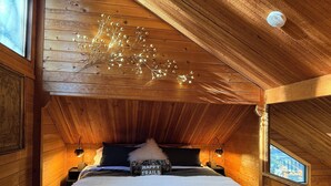 Ein gemütliches Schlafzimmer in einer Holzhütte mit Bett, Kissen, einer Bank und einer dekorativen Lampe.