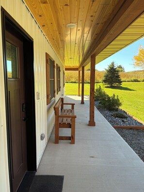 Eine überdachte Veranda mit einer Bank, einer Tür und Blick auf ein grünes Feld.