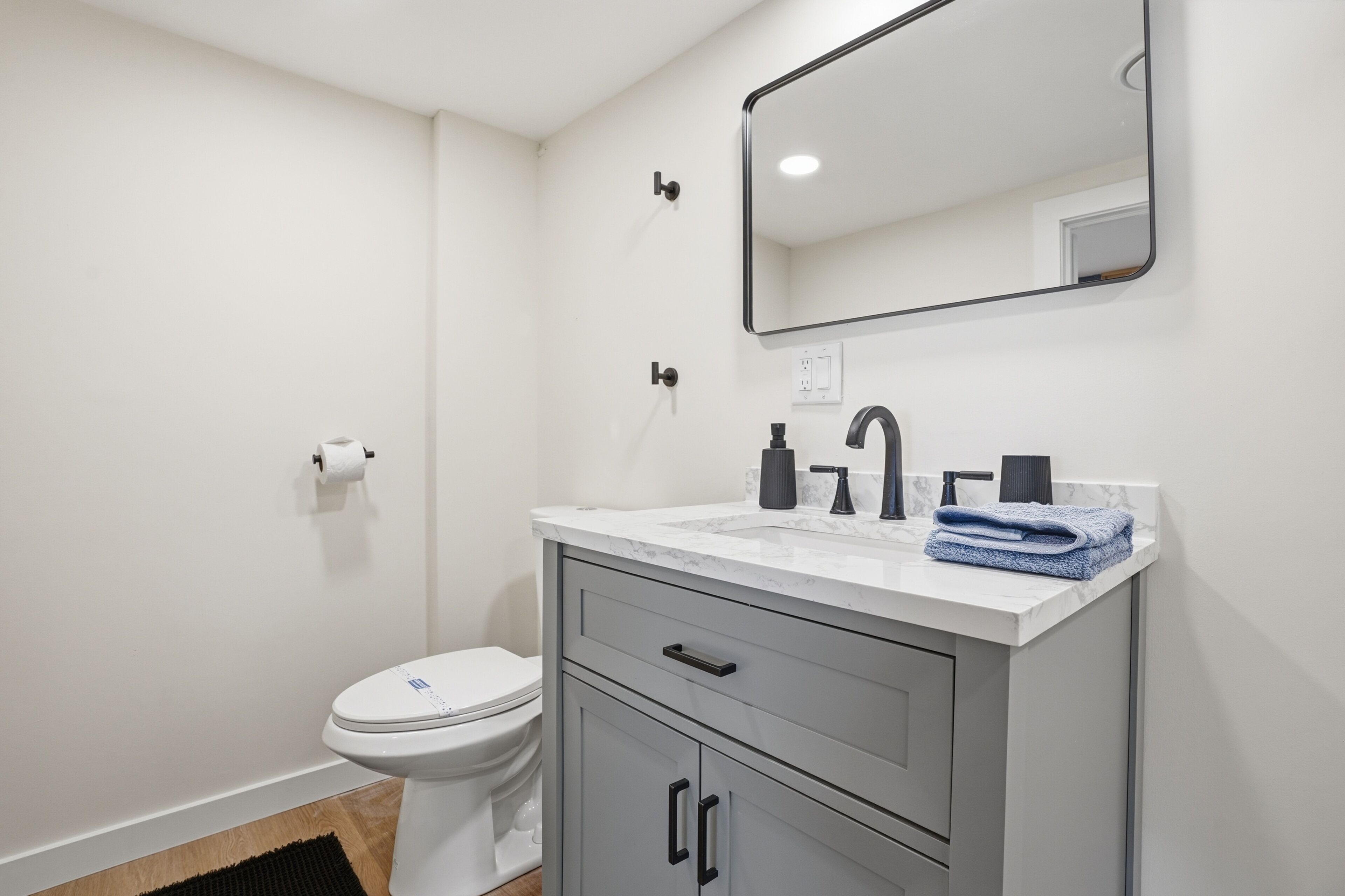 A bathroom with a toilet, sink, mirror, and cabinets.
