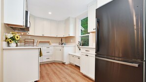 Una cucina moderna con mobili bianchi, un frigorifero in acciaio inossidabile e un pavimento in legno.