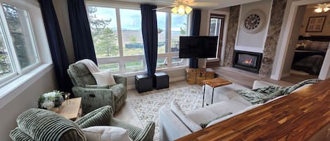 Una sala de estar con chimenea, televisor y vistas al exterior.