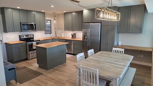 A modern kitchen with grey cabinets, stainless steel appliances, a wooden island, and a dining area with a wooden table and white chairs. - New Listing! True ski-in/out newly remodeled all-four seasons mountainside condo (Granby)