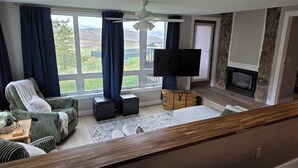 A living room with a large window, a flat-screen TV, a fireplace, and a stone accent wall. - New Listing! True ski-in/out newly remodeled all-four seasons mountainside condo (Granby)