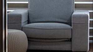 En grå sofa med tilhørende skammel, placeret foran persienner.
