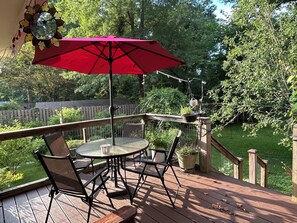 A wooden deck with a table and chairs, a red umbrella, and a hanging planter.