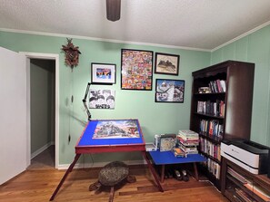 A room with a wooden floor, a desk with a blue top, a bookshelf, and a turtle on the floor.