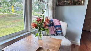 Ein Zimmer mit Holztisch, Blumen in einer Vase, einer Couch und einem Gemälde an der Wand.
