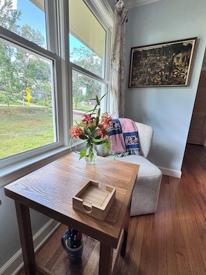 Ein Zimmer mit Holztisch, Blumen in einer Vase, einer Couch und einem Gemälde an der Wand.