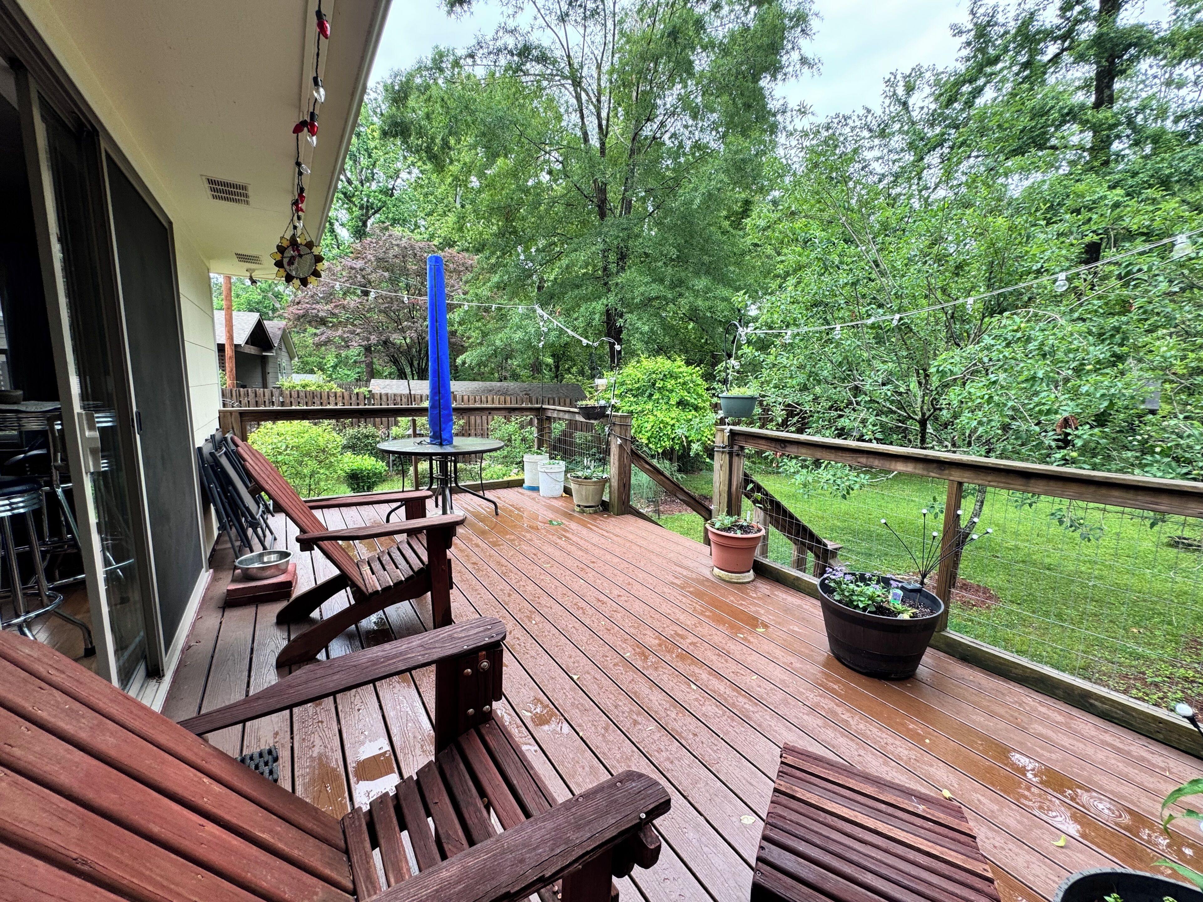 A wooden deck with outdoor furniture, a blue umbrella, and potted plants.