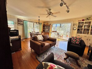 A living room with a brown sofa, a patterned rug, a ceiling fan, and a bookshelf.