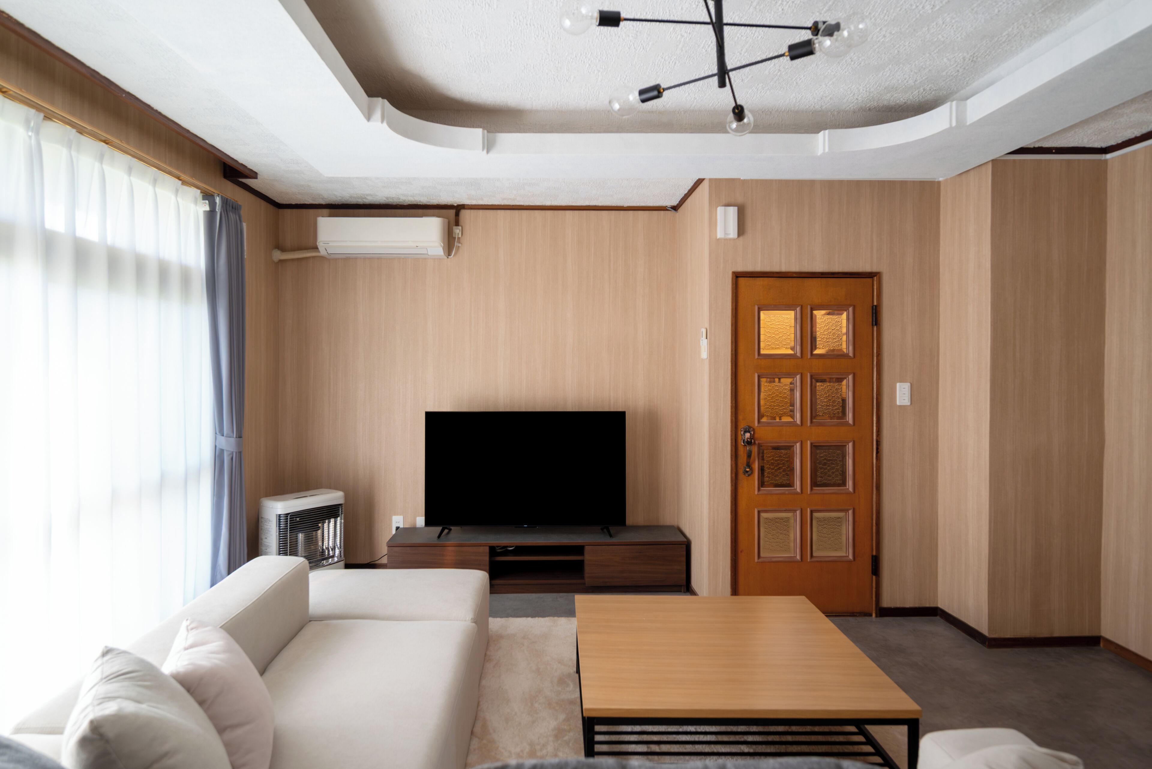 A modern living room with a flat-screen TV, a sofa, a coffee table, and a wooden door.