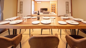 A dining table set for six with plates, cutlery, and glasses, a bottle of wine, and a television in the background. - Kamifurano Cozy House (Kamifurano-cho, Sorachi District)