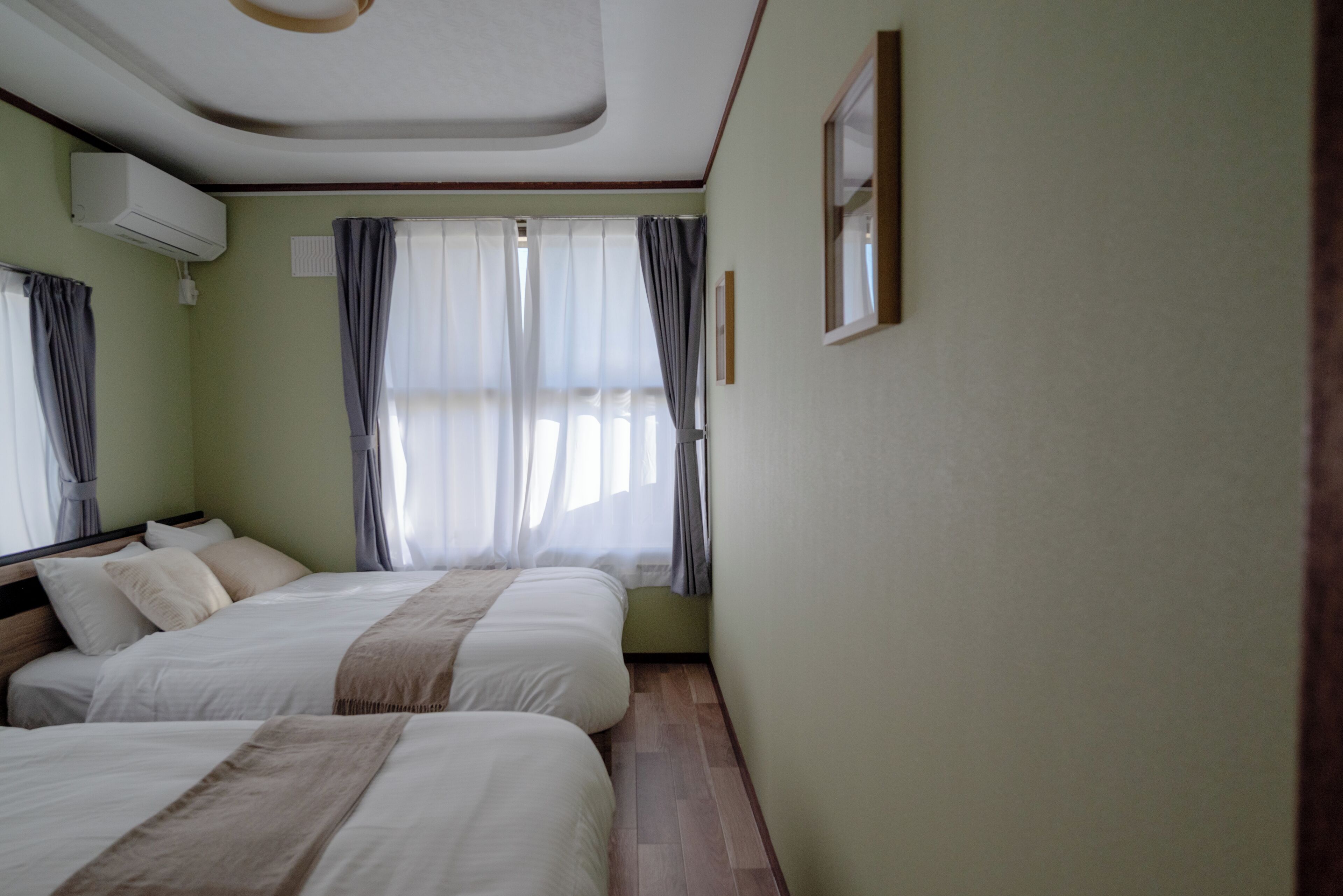 Una habitación con dos camas, una ventana con cortinas, un aire acondicionado y un cuadro en la pared.