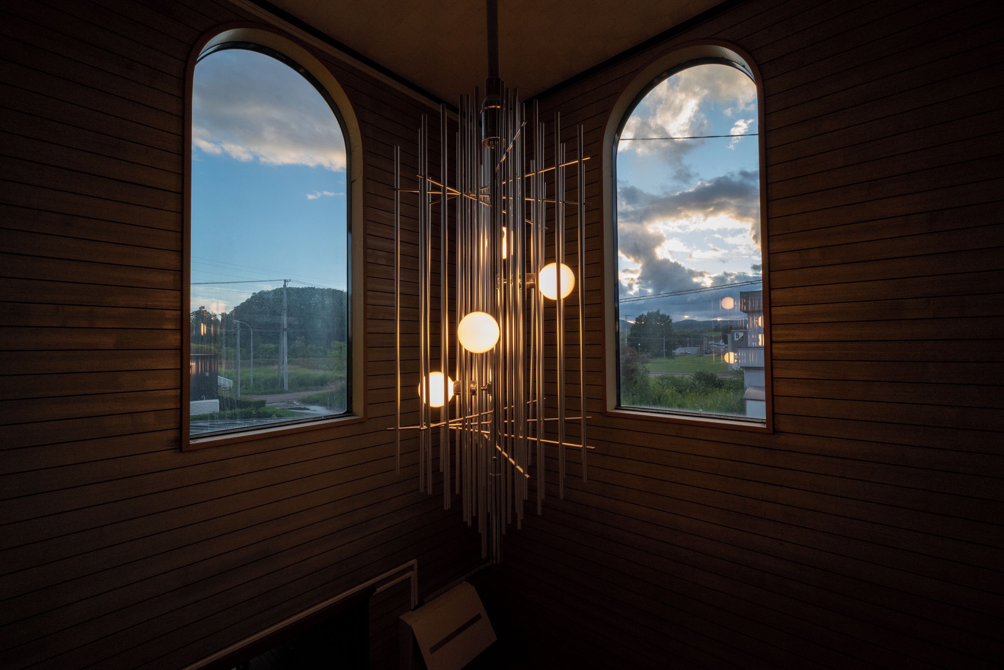 A room with wooden paneling, two arched windows, and a modern light fixture.