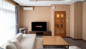 A modern living room with a flat-screen TV, a sofa, a coffee table, and a wooden door. - Kamifurano Cozy House (Kamifurano-cho, Sorachi District)