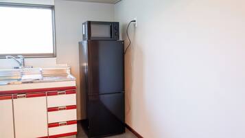 A compact kitchen with a refrigerator, microwave, and a window above the sink.