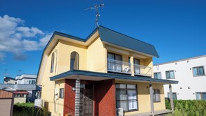 A two-story residential building with a balcony, a visible antenna, and a small attached garage. - Kamifurano Cozy House (Kamifurano-cho, Sorachi District)