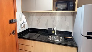 A compact kitchen with a microwave, a sink, and wooden cabinets. - Beachfront Studio in Piatã | Incredible View, Wi-Fi, Smart TV and Garage (Salvador)