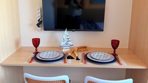A dining area with a TV mounted on the wall, two wicker chairs, a table set with plates, cutlery, and red glasses. - Beachfront Studio in Piatã | Incredible View, Wi-Fi, Smart TV and Garage (Salvador)