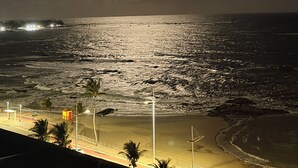 A beach at night with a bright moon, ocean waves, and a distant shoreline with lights. - Beachfront Studio in Piatã | Incredible View, Wi-Fi, Smart TV and Garage (Salvador)