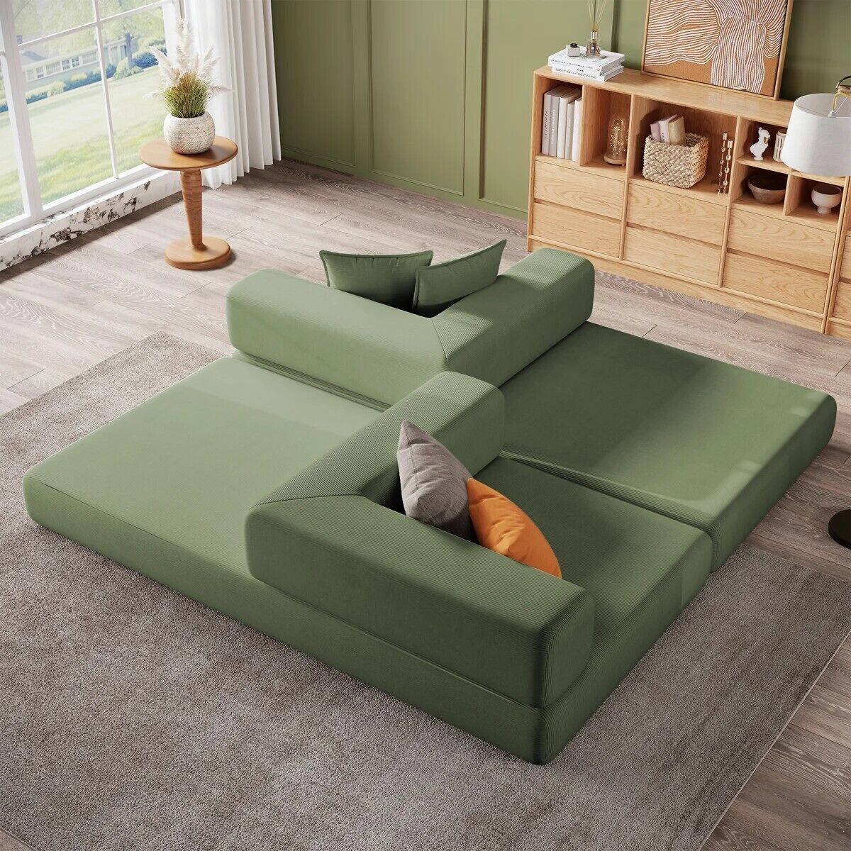 Un sofá seccional verde con cojines, una mesita auxiliar con una planta y un estante de madera con libros y objetos decorativos.