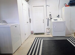 A laundry room with a washing machine, dryer, and a vacuum cleaner. - 2BR Pet-Friendly Clearwater home. Private Yard and Short drive to TPA & Beaches. (Clearwater)