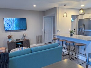 A modern kitchen with a built-in refrigerator, bar stools, and a flat-screen TV mounted on the wall. - 2BR Pet-Friendly Clearwater home. Private Yard and Short drive to TPA & Beaches. (Clearwater)