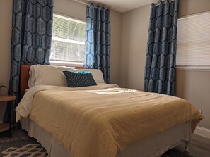 A bedroom with a bed, curtains, a window, and a bedside table. - 2BR Pet-Friendly Clearwater home. Private Yard and Short drive to TPA & Beaches. (Clearwater)