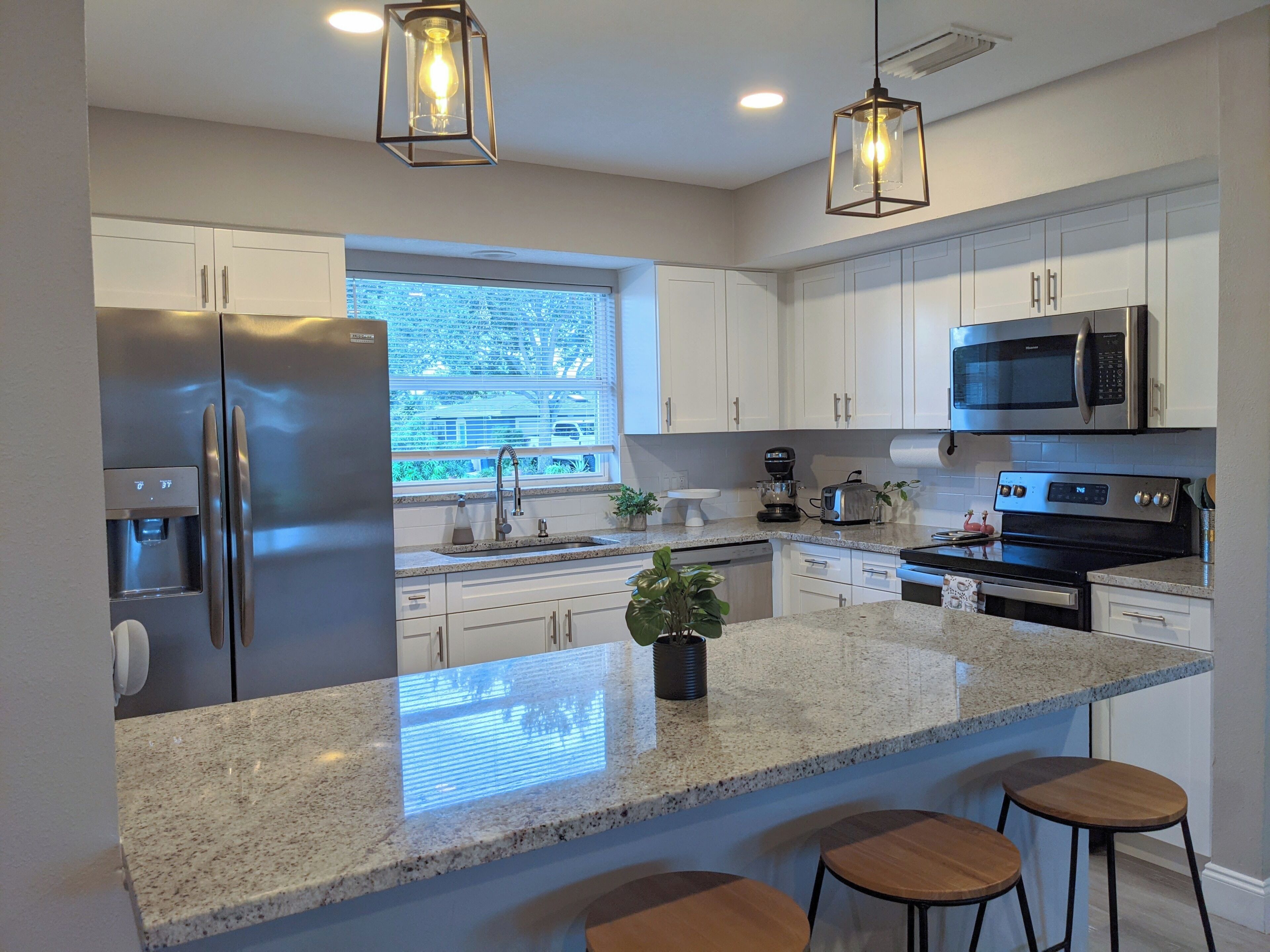 A modern kitchen with stainless steel appliances, granite countertops, and bar stools.