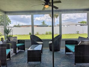 Eine überdachte Terrasse mit Korbmöbeln, einem Deckenventilator und Blick auf einen grünen Garten.