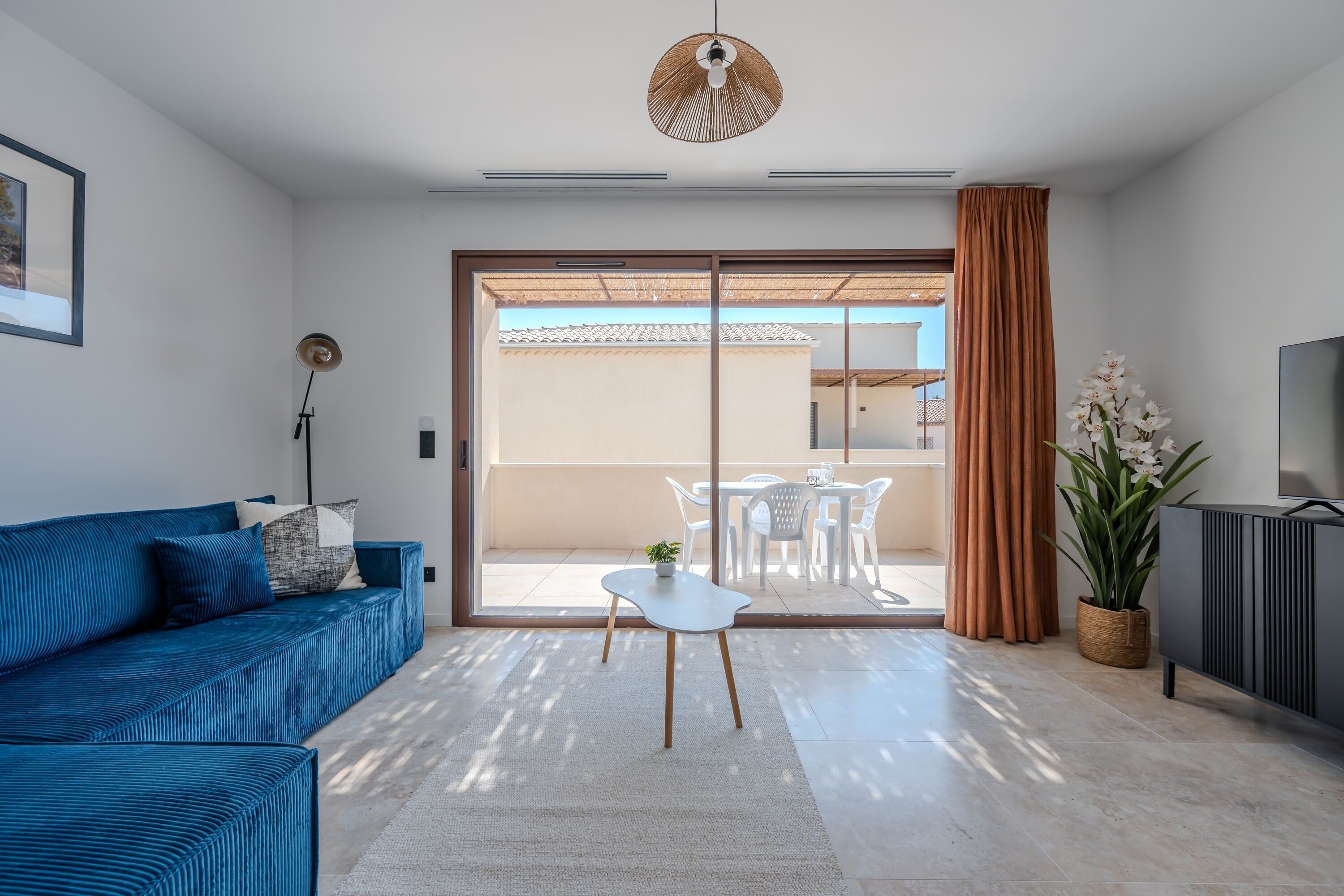 Un salon moderne avec un canapé, une petite table, une plante en pot et une porte-fenêtre coulissante donnant sur un espace extérieur.
