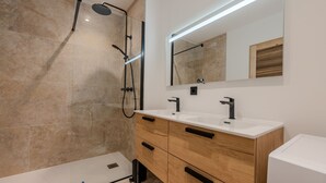 Une salle de bain moderne avec une douche en verre, deux vasques, des meubles en bois et un grand miroir.