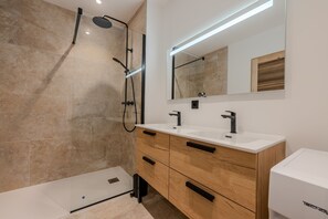 A modern bathroom with a glass-enclosed shower, two sinks, wooden cabinets, and a large mirror. - Le Cocon des Taillades - Appt climatisé (Taillades)