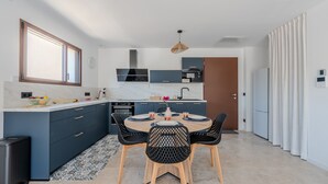 Une cuisine moderne avec un coin repas, dotée d’une grande fenêtre, d’appareils électroménagers intégrés et d’un îlot central.