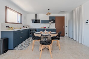 A modern kitchen with a dining area, featuring a large window, built-in appliances, and a central island. - Le Cocon des Taillades - Appt climatisé (Taillades)