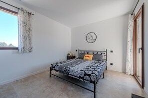 Um quarto com uma cama, uma mesa de cabeceira, um relógio na parede e uma janela com cortinas.