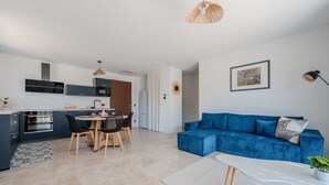 Une cuisine moderne avec des meubles de couleur sombre, un coin repas avec une table ronde et des chaises, un canapé bleu et une table basse blanche.