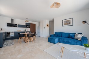 A modern kitchen with dark cabinetry, a dining area with a round table and chairs, a blue sofa, and a white coffee table. - Le Cocon des Taillades - Appt climatisé (Taillades)