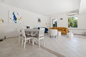A modern living room with a dining area, white walls, and artwork. - Le Mas des Aromes - Piscine Privée (Mandelieu-la-Napoule)