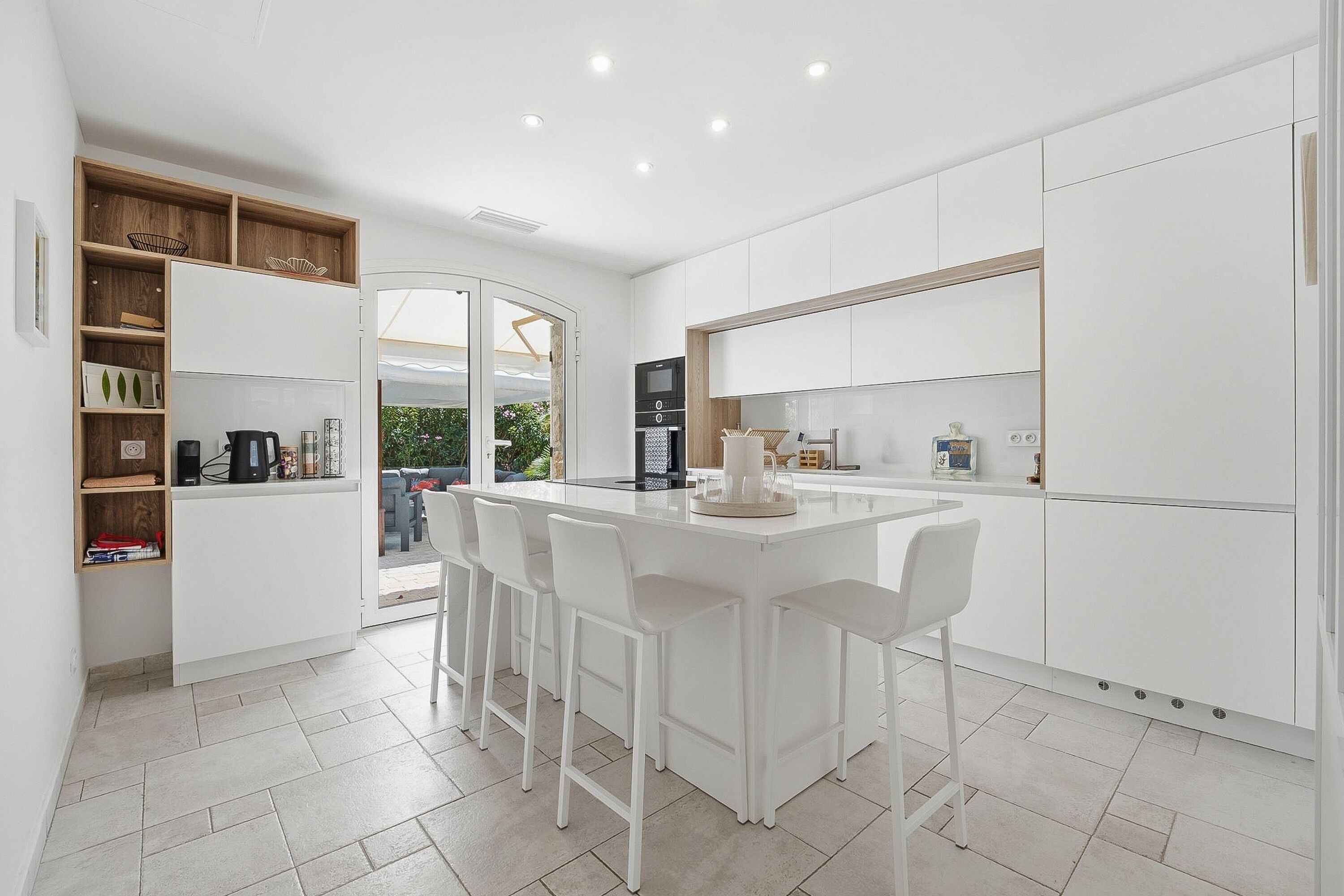 A modern kitchen with white cabinetry, a central island with bar stools, and a built-in oven.