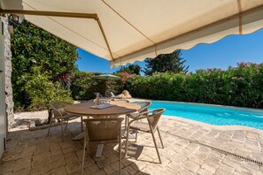 A patio with a table and chairs, a pool, and a covered area. - Le Mas des Aromes - Piscine Privée (Mandelieu-la-Napoule)