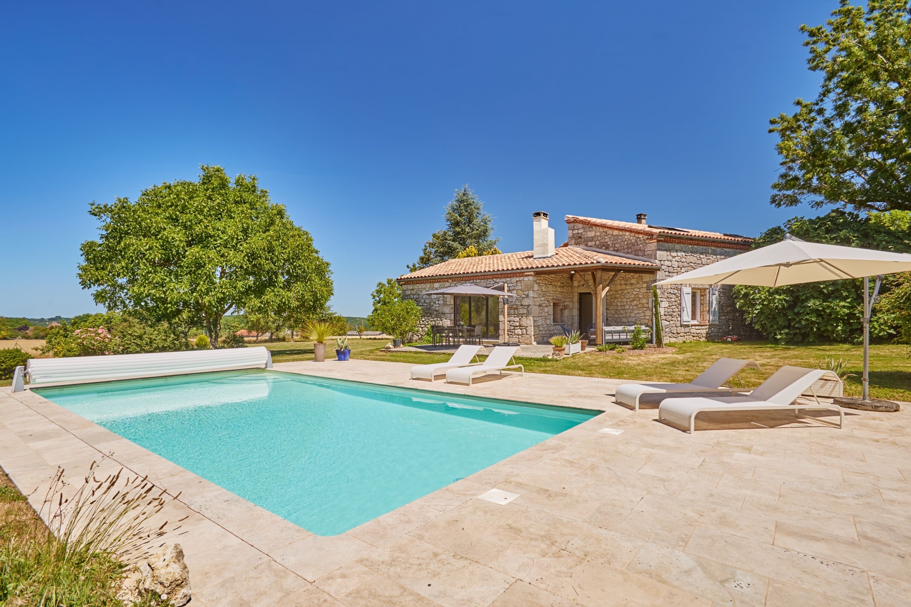 A stone house with a swimming pool, lounge chairs, and a patio area.