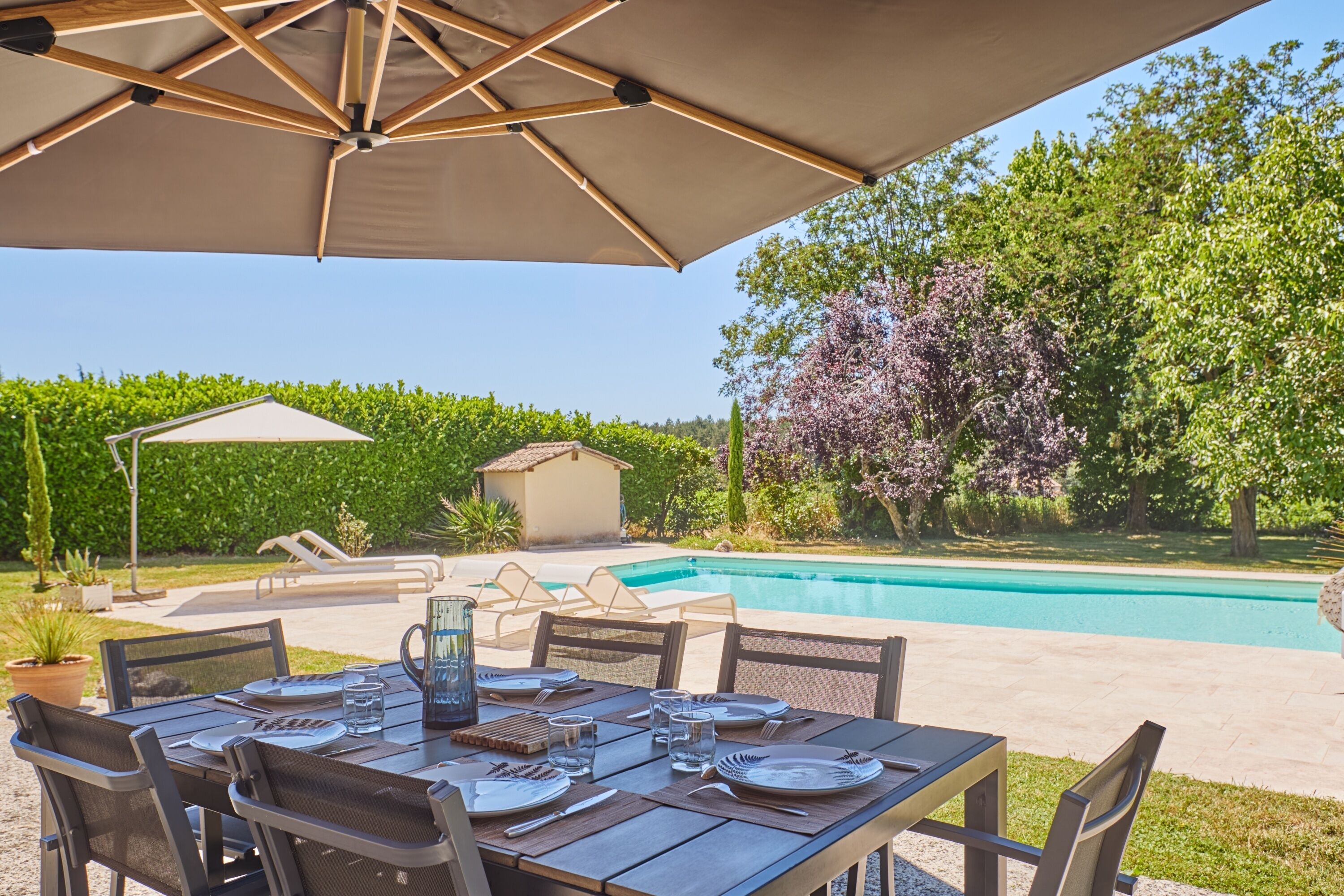 An outdoor dining area with a table set for four, surrounded by chairs, under a large umbrella.