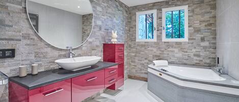 A modern bathroom with a large round mirror, a vessel sink, a red vanity, and a freestanding bathtub.