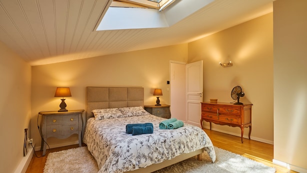 A bedroom with a skylight, a bed with floral bedding, two bedside lamps, a dresser, and a white rug. - Le Mounet, charmante maison dans le Pays de Serres (Frespech)