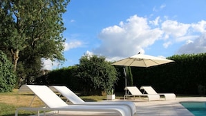 A poolside area with lounge chairs and a large umbrella. - Le Mounet, charmante maison dans le Pays de Serres (Frespech)
